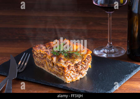 heiß dampfende Lasagne mit Rotwein auf Schiefer und Holz Tisch Stockfoto