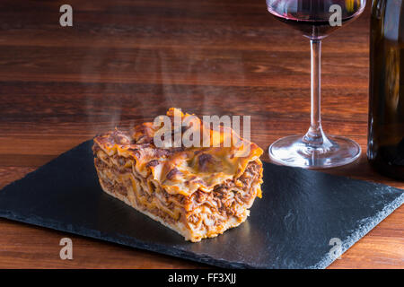 frische heiße dampfende Lasagne Pasta serviert am Tisch aus Holz und Schiefer Platte Stockfoto