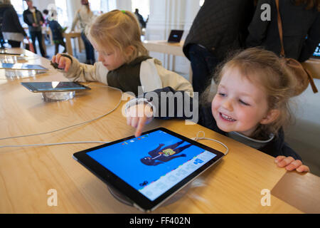 Drei Jahre altes Mädchen / Kind / Kinder, glücklich & lächelnd zu sein mit einem iPad i Pad tablet-Computer. Apple Store Amsterdam Niederlande. Stockfoto