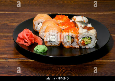 Verschiedene Sushi auf der schwarzen Platte auf braunem Hintergrund Stockfoto