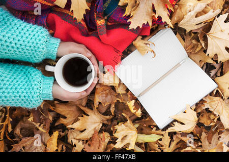 Frau Hände halten Tasse Kaffee über Blätter Hintergrund. Ansicht von oben Stockfoto