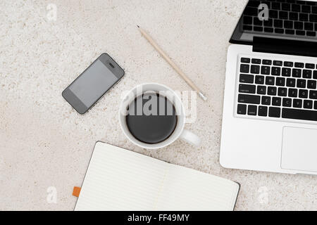 Laptop, Smartphone-Tasse Kaffee und Notebook befindet sich im Teppich Hintergrund, Ansicht von oben Stockfoto
