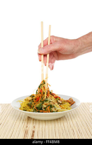 Hand mit Stäbchen eintauchen in eine Schüssel mit Singapur Nudeln vor einem weißen Hintergrund Stockfoto