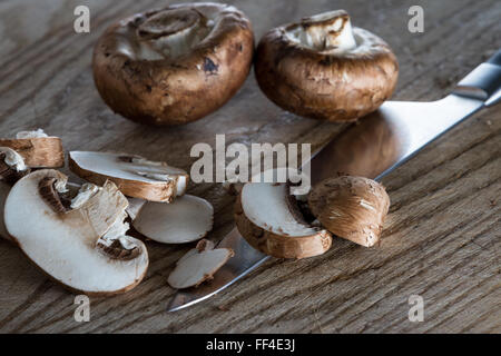 Nahaufnahme von einem Köche Hände schneiden rohe Pilze auf einem Holzbrett Stockfoto