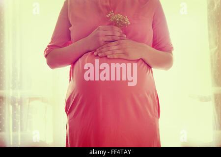 Closeup auf Bauch der schwangeren Frau, hält in Händen Blumenstrauß Stockfoto