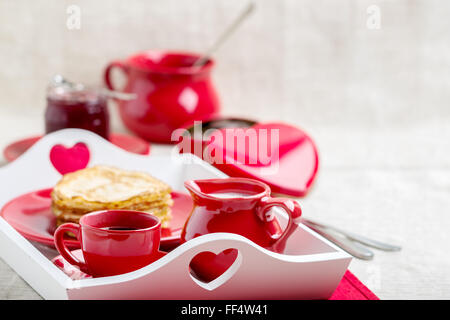 Frühstück. Pfannkuchen und Kaffee mit Milch auf einem Tablett zum Valentinstag. Selektiven Fokus. Stockfoto