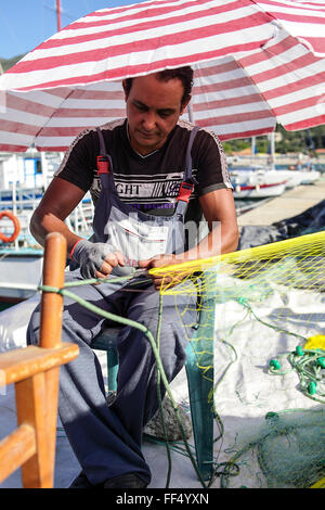 Griechische Fischer seine Netze zu reparieren, während sich die Sonnen-Strahlen schützen am Valtos Beach Hafenmole gelegen. Stockfoto
