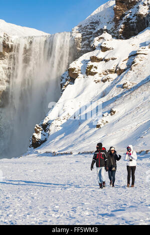 Touristen am Wasserfall Skogafoss, Südisland im Januar mit gefrorenen Eiszapfen Stockfoto