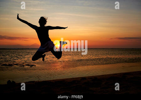 Silhouette einer Frau, die einen Sprung in der Luft, vor einem Sonnenuntergang Himmel gesehen. Stockfoto