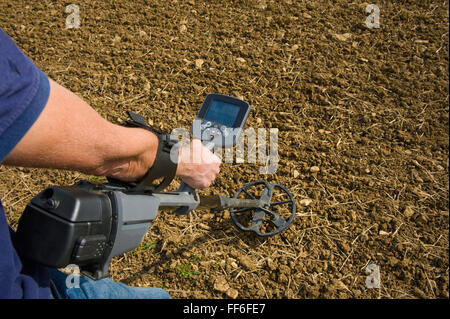 Ein Mann hält einen Metalldetektor knapp über dem Boden in einem Acker auf der Suche nach Metallobjekten. Stockfoto