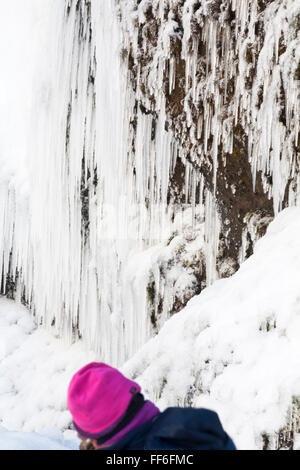 Kontrastierender pinkfarbener Besucherhut mit gefrorenen Eiszapfen am Wasserfall Skogafoss, Südisland im Januar Stockfoto