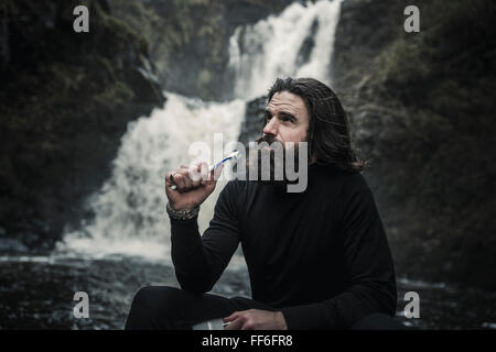 Wildes Campen. Ein Mann hält eine Zahnbürste von Wasser über die Felsen Rauschen. Stockfoto