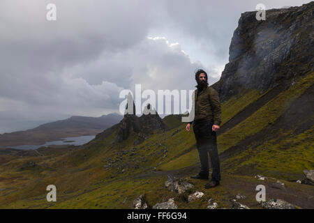 Ein Mann auf einem schmalen Weg zu einer dramatischen Landschaft von Felsen Zinnen unter bedecktem Himmel mit niedrigen Wolken steigen. Stockfoto