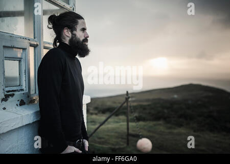 Ein Mann vor einem Gebäude stehen, schaut in den dunkler werdenden Himmel bei Sonnenuntergang. Stockfoto