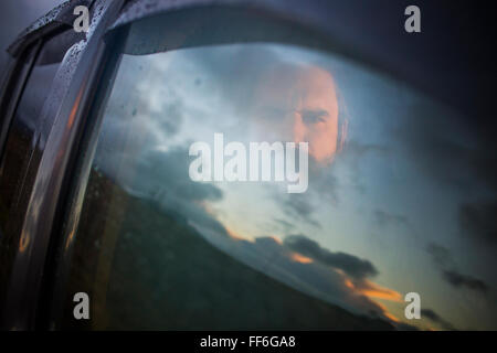 Ein Mann sitzt in einem Auto auf der Suche. Reflexionen auf den Sonnenuntergang Himmel auf das Fenster. Stockfoto