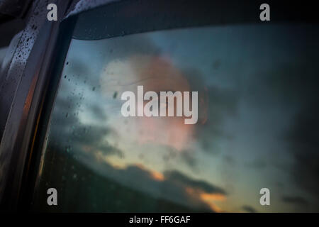 Ein Mann sitzt in einem Auto auf der Suche. Reflexionen auf den Sonnenuntergang Himmel auf das Fenster. Stockfoto