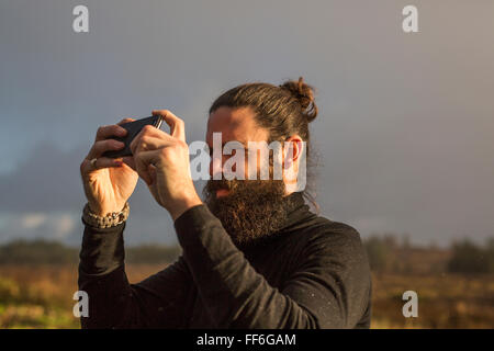 Ein Mann stehend mit einem Smartphone ein Foto unter einem grauen Himmel zu nehmen. Stockfoto