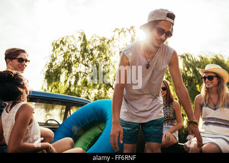 Porträt von glücklichen jungen Freunde gehen auf eine Reise. Junge Männer und Frauen auf der Rückseite einen Pickup-Truck mit aufblasbaren Schläuchen. Stockfoto