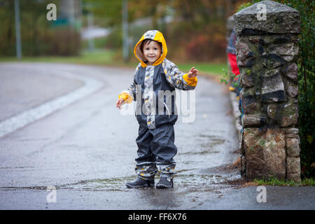 Süsser Boy im Park, spielen im Regen, springen in Pfützen, Spritzwasser Stockfoto