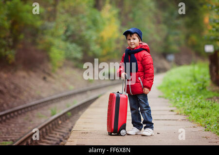 Liebenswert niedlich kleine Kind, junge, die Wartezeit auf einen Bahnhof auf einen Zug mit Koffer, Herbst Stockfoto