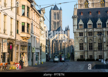 Blick auf die Straße im historischen Zentrum von Gent, Belgien.  Zwei elektrische Straßenbahnen fahren Sie entlang des Straßenbahnnetzes vorbei die schöne Architektur mit St.-Nikolaus-Kirche im Hintergrund. Stockfoto