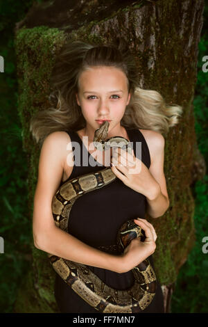 Porträt eines liegenden schönen jungen Mädchens mit Schlange in einem Wald Stockfoto