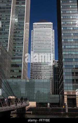 Pendler Fuß über die South Quay Fußgängerbrücke über das Süd-Dock auf der Themse in Canary Wharf, East London, England, Vereinigtes Königreich. Canary Wharf ist ein Symbol des Londoner Finanzsektors und die berühmte Wolkenkratzer One Canada Square im Hintergrund zu sehen. Stockfoto