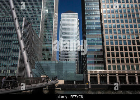 Pendler Fuß über die South Quay Fußgängerbrücke über das Süd-Dock auf der Themse in Canary Wharf, East London, England, Vereinigtes Königreich. Canary Wharf ist ein Symbol des Londoner Finanzsektors und die berühmte Wolkenkratzer One Canada Square im Hintergrund zu sehen. Stockfoto