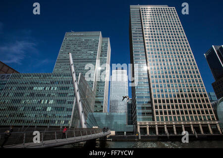 Pendler Fuß über die South Quay Fußgängerbrücke über das Süd-Dock auf der Themse in Canary Wharf, East London, England, Vereinigtes Königreich. Canary Wharf ist ein Symbol des Londoner Finanzsektors und die berühmte Wolkenkratzer One Canada Square im Hintergrund zu sehen. Stockfoto