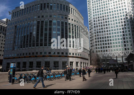 Stadtarbeiter überqueren Sie den Platz vor dem Thompson Reuters Gebäude um 30 South Kolonnade, Canary Wharf, Docklands, London, Vereinigtes Königreich. Es gibt eine Reihe von Barclay es Boris Bikes die Londoner verwenden, um Reisen quer durch die Stadt. Die Sonne leuchtet One Canada Square, wahrscheinlich der berühmtesten Wolkenkratzer in London. Stockfoto