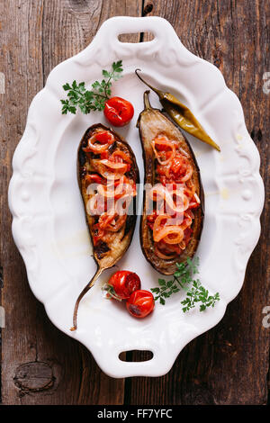 Gebackene Aubergine gefüllt mit Gemüse (Imam Bayildi). Elegante weiße Platte auf alten Holzbrett. Stockfoto