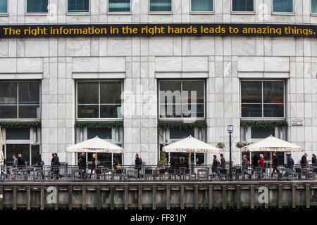 "Die richtige Informationen in die richtigen Hände führt zu erstaunlichen Dinge" auf der Live-Ticker der Reuters Gebäude über ein All Bar One Restaurant in Canary Wharf, London, England, Unite Kingdom geschrieben.  Stadtarbeiter Fuß am Gebäude vorbei auf einem Pfad an der Themse. Stockfoto