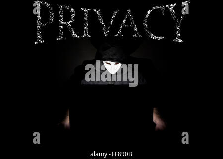 Ein maskierter Mann auf einen Laptop als Symbol für die Gefahren des Internets. Stockfoto