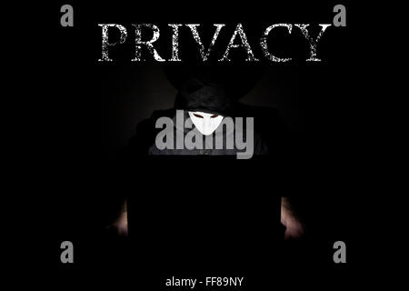 Ein maskierter Mann auf einen Laptop als Symbol für die Gefahren des Internets. Stockfoto