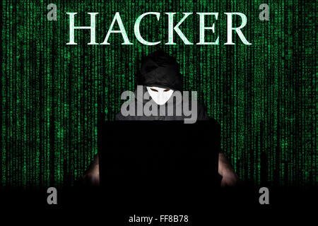 Ein maskierter Mann auf einen Laptop als Symbol für die Gefahren des Internets. Stockfoto