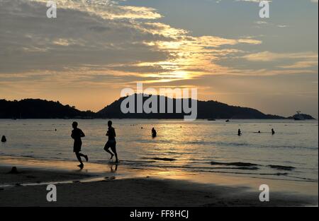 Phuket, Thailand: Jogger und Schwimmer am Patong Beach während einer dramatischen Sonnenuntergang über der Andamanensee Stockfoto