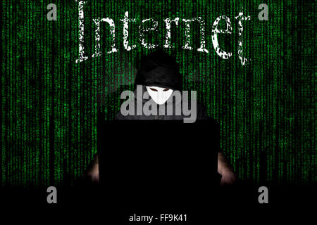 Ein maskierter Mann auf einen Laptop als Symbol für die Gefahren des Internets. Stockfoto