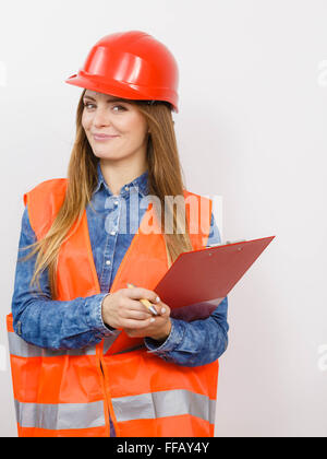 Frau Bau Arbeiter Builder strukturelle engineerin in rot orange Weste schwer Helm hält Stift Datei Pad. Sicherheit in der industriellen Stockfoto