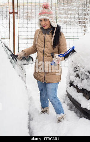 Stets gut gelaunte Frau Schnee vom Auto in kalten Tag Reinigung Stockfoto