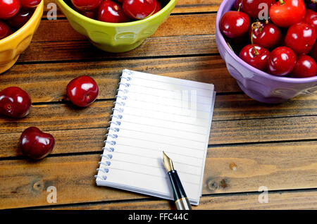 Notebook und bunte Schale mit Kirschen auf Tisch Stockfoto