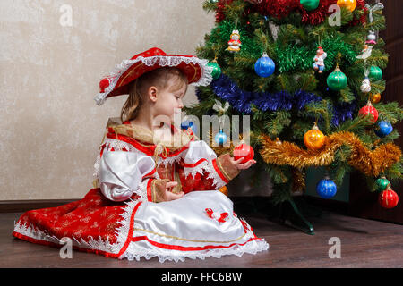 kleines Mädchen im Karnevalskostüm hält eine Weihnachtskugel Stockfoto