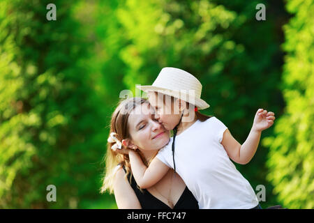 Tochter umarmt ihre Mutter auf dem Hintergrund der hellen saftig grünem Laub. Glückliche Familie. Mutter und Kind Mädchen. Platz für Text. Stockfoto
