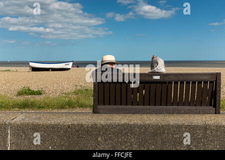 Mittleren Alters paar sitzt auf einer Bank an der Küste von Aldeburgh, Suffolk, UK Stockfoto