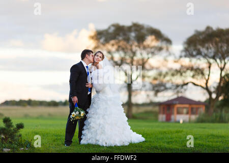 Glückliches Hochzeitspaar zu Fuß entlang der Bereich umarmen und küssen am Abend Stockfoto