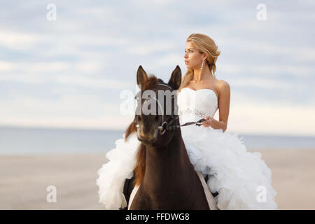 Braut auf einem Pferd am Meer in ihrem Hochzeitstag Stockfoto