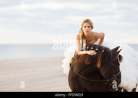 Braut auf einem Pferd am Meer in ihrem Hochzeitstag Stockfoto