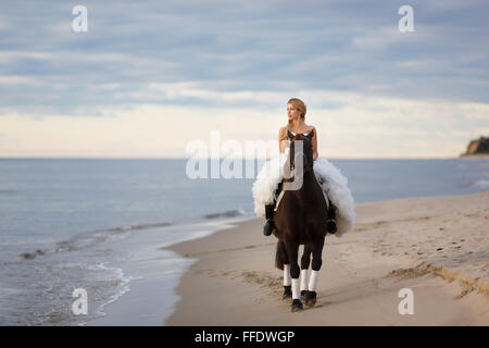 Braut auf einem Pferd am Meer in ihrem Hochzeitstag Stockfoto
