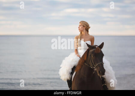 Braut auf einem Pferd am Meer in ihrem Hochzeitstag Stockfoto
