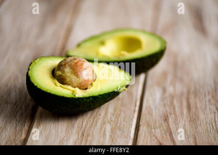 eine Avocado Kürzung der Hälften damit Saatgut auf einer rustikalen Holzoberfläche Stockfoto