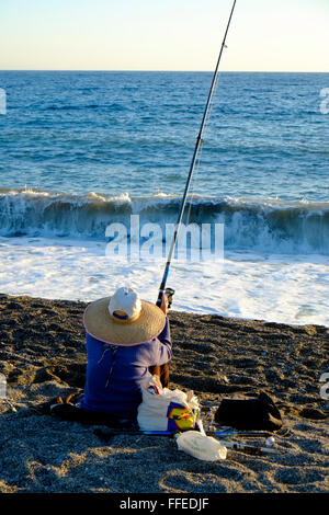 Eingeflügelter Angler, der am Strand sitzt und angeln kann, wenn die Sonne untergeht. Almuñécar, Granada, Andalusien. Spanien Stockfoto